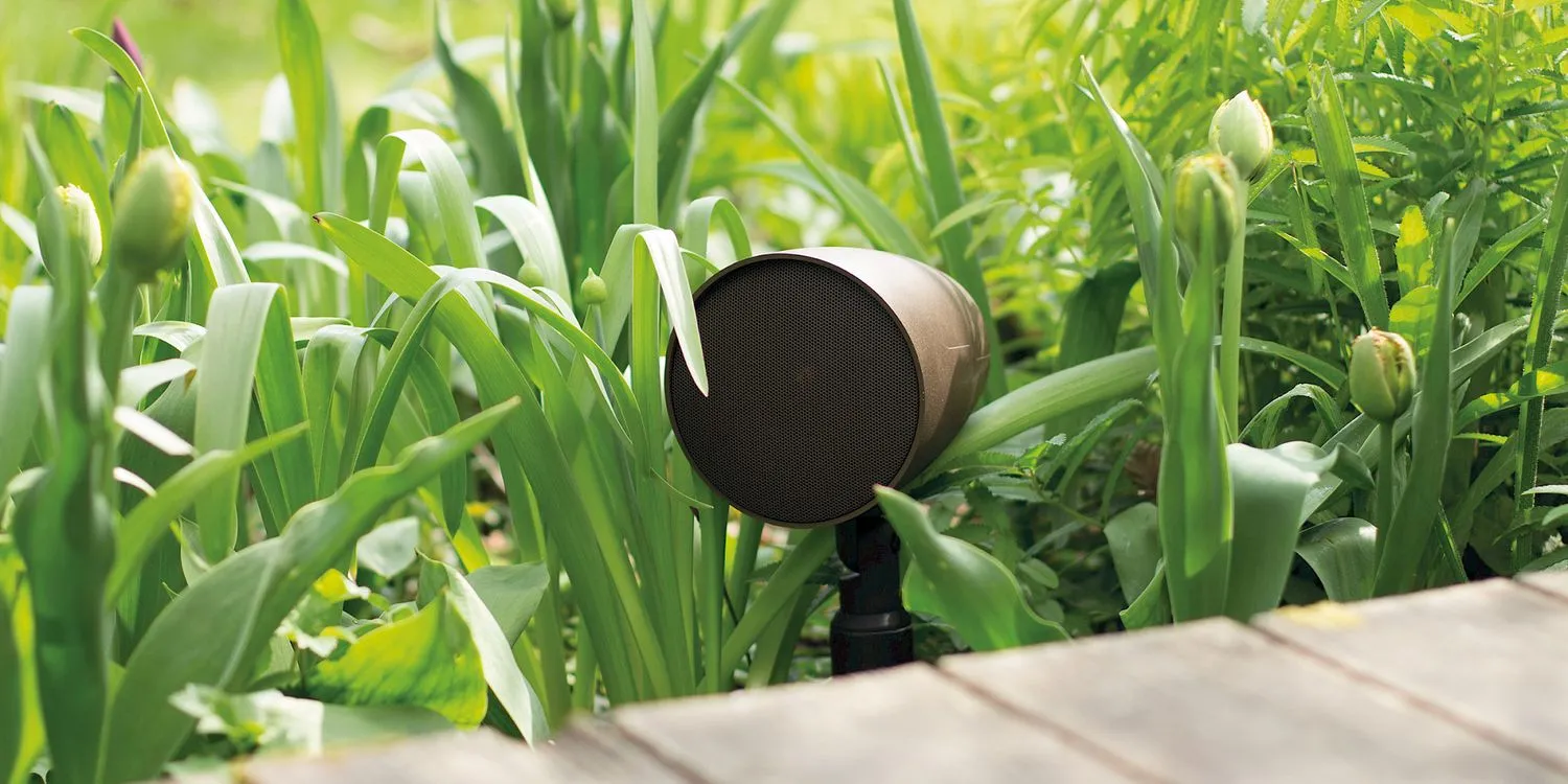 Weatherproof Monitor Audio garden speaker nestled among tulips beside a wooden deck